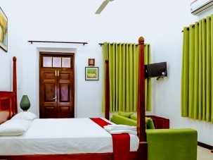 The spacious Lemon Grass Room at Flamingo Villa in Jaffna, offering air conditioning, a wardrobe, a private bathroom with a shower and bidet, a tiled floor, and a flat-screen TV with cable channels. The room features a comfortable double bed for a restful stay.
