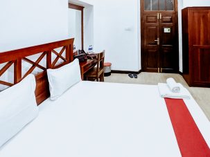 The elegant bedroom in the Gloriosa Room at Flamingo Villa in Jaffna, featuring a comfortable double bed, air conditioning, a wardrobe, tiled flooring, and a flat-screen TV with cable channels for a pleasant stay.